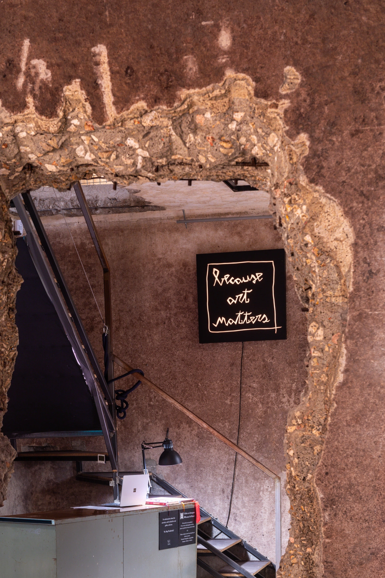 Raw concrete archway entrance at Because Art Matters gallery in Lisbon, showing the modern office and exhibition area.